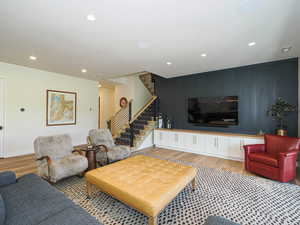 Living room featuring stairs, recessed lighting, light wood-type flooring, an accent wall, and a decorative wall