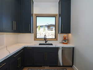 Kitchen featuring dishwasher, light stone counters, dark cabinetry, and wood finished floors