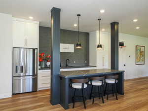 Kitchen featuring stainless steel fridge, white cabinetry, a kitchen breakfast bar, recessed lighting, and light wood-style flooring