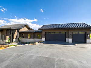 View of front of house featuring stone siding, a garage, driveway, and a metal roof