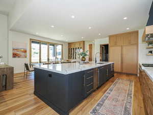 Kitchen featuring recessed lighting, light wood-type flooring, ventilation hood, a large island with sink, and light stone countertops