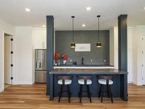Kitchen featuring dark countertops, stainless steel refrigerator with ice dispenser, a breakfast bar area, and recessed lighting