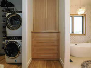 Washroom with stacked washer / dryer, a chandelier, and wood finished floors