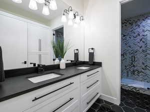 Bathroom featuring double vanity, tiled shower, a chandelier, and tile patterned flooring