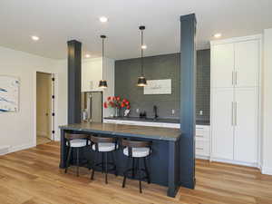 Kitchen featuring dark countertops, a breakfast bar, stainless steel refrigerator with ice dispenser, light wood-type flooring, and white cabinetry