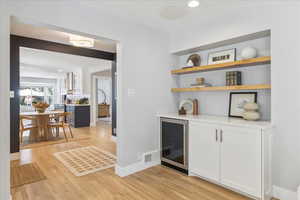 Indoor bar featuring wine cooler, light wood finished floors, and recessed lighting