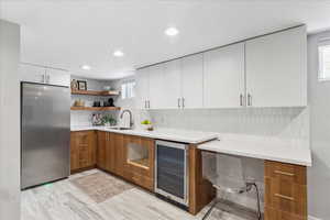 Kitchen with freestanding refrigerator, open shelves, beverage cooler, white cabinets, and light countertops