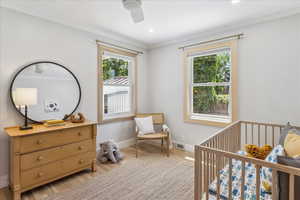 Bedroom with ornamental molding, light wood-style flooring, a crib, and a ceiling fan