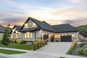 View of front facade with board and batten siding, roof with shingles, stone siding, an attached garage, and a yard