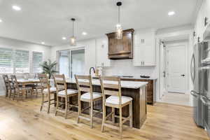 Kitchen with recessed lighting, a kitchen island with sink, light wood-style flooring, white cabinets, and a breakfast bar area