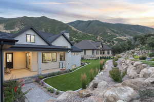 Back of house with stucco siding, a chimney, a mountain view, a yard, and a shingled roof