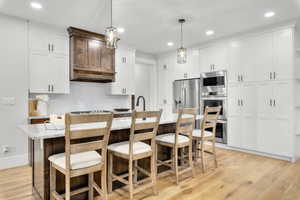 Kitchen with light wood-type flooring, a breakfast bar, appliances with stainless steel finishes, recessed lighting, and white cabinetry