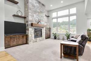 Carpeted living area featuring a stone fireplace, wood finished floors, recessed lighting, and a towering ceiling