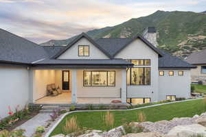 Back of property at dusk with roof with shingles, a chimney, and stucco siding