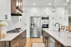 Kitchen with stainless steel appliances, white cabinets, light wood-style flooring, hanging light fixtures, and recessed lighting