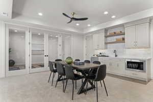 Dining space with recessed lighting, ceiling fan, light colored carpet, bar with sink, and a tray ceiling