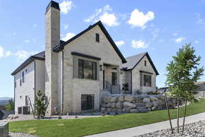 View of front facade with stone siding, a chimney, and a front lawn