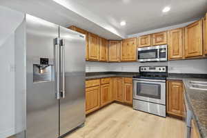 Kitchen featuring appliances with stainless steel finishes, light wood-style floors, recessed lighting, and brown cabinets