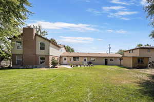 Back of house featuring a patio area, a chimney, brick siding, a yard, and an outbuilding