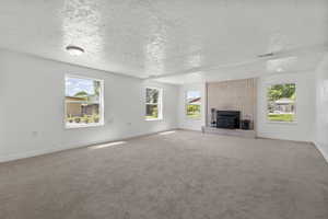 Unfurnished living room featuring plenty of natural light, a textured ceiling, carpet, and a brick fireplace