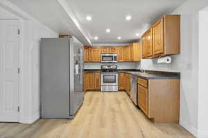 Kitchen with appliances with stainless steel finishes, dark countertops, recessed lighting, light wood-style flooring, and brown cabinets
