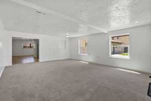 Empty room featuring carpet floors, plenty of natural light, a textured ceiling, and beam ceiling