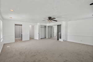 Unfurnished bedroom featuring light colored carpet, two closets, a ceiling fan, and a textured ceiling