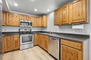 Kitchen with appliances with stainless steel finishes, light wood finished floors, dark countertops, recessed lighting, and brown cabinetry
