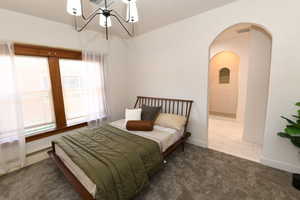 Carpeted bedroom with a chandelier, a baseboard heating unit, and arched walkways
