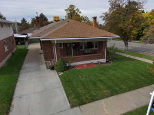 Bungalow-style house featuring a porch, a front lawn, brick siding, roof with shingles, and a chimney