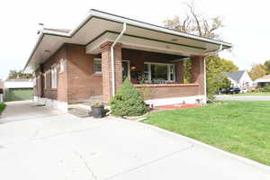 View of front facade featuring brick siding, a front yard, covered porch, and a detached garage