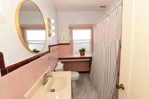 Full bath featuring healthy amount of natural light, tile walls, a wainscoted wall, a shower with curtain, and vanity