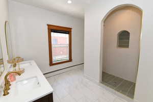 Bathroom with double vanity, baseboard heating, tiled shower, and recessed lighting