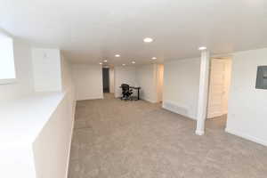 Basement featuring light colored carpet, electric panel, and recessed lighting