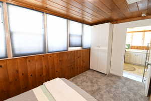 Bedroom with light colored carpet, wooden ceiling, wooden walls, and ensuite bath