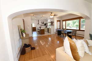 Living room featuring arched walkways, light wood-type flooring, baseboard heating, and ceiling fan