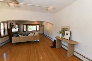 Living room featuring arched walkways, track lighting, light wood-style floors, a baseboard radiator, and a textured ceiling