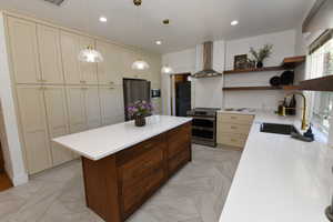 Kitchen with open shelves, appliances with stainless steel finishes, wall chimney exhaust hood, light stone countertops, and recessed lighting