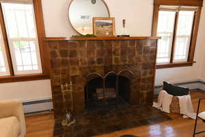 Detailed view of a tiled fireplace, wood finished floors, baseboard heating, and a baseboard radiator