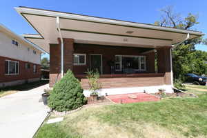 Rear view of property featuring brick siding, a lawn, and a porch