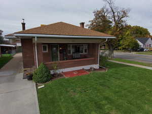 Bungalow-style house featuring covered porch, a front lawn, a chimney, and brick siding