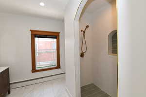 Full bath with tiled shower, a baseboard heating unit, and vanity