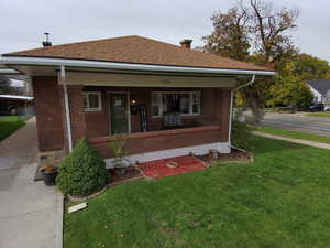Bungalow-style home with a porch, a front yard, a chimney, brick siding, and roof with shingles
