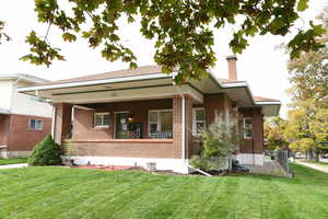 Rear view of house featuring a lawn, a porch, a chimney, and brick siding