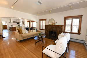 Living room with track lighting, arched walkways, light wood-type flooring, a fireplace, and a baseboard radiator