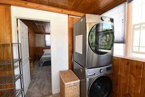 Laundry room featuring estacked washer and dryer, wood walls, wooden ceiling, and carpet