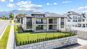 Rear view of house featuring a balcony, stone siding, a fenced backyard, and roof with shingles