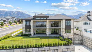 Rear view of property with a balcony, a fenced front yard, a mountain view, and roof with shingles