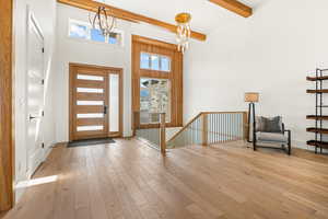 Foyer with a chandelier, healthy amount of natural light, a high ceiling, wood-type flooring, and beamed ceiling