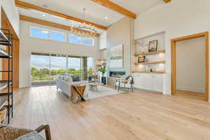 Living room with beam ceiling, light wood finished floors, a chandelier, a glass covered fireplace, and a high ceiling
